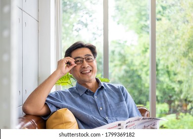 Selective focus at face. Senior Asian man reading newspaper mock up at the sofa couch while drinking coffee in the morning. Happy retirement with relaxation lifestyle and routine. - Powered by Shutterstock