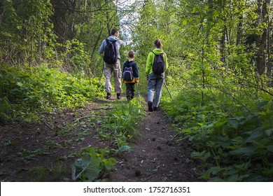 Selective focus. Father with two children with backpacks and sticks walk along forest path in summer. Family weekend outdoors in woods, camping. Hiking with kids, lifestyle. Social distancing together