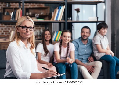 Selective Focus Of Female Counselor Writing In Clipboard On Therapy Session With Family 