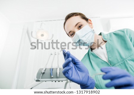 selective focus of female dentist in mask and latex gloves holding dental instrument