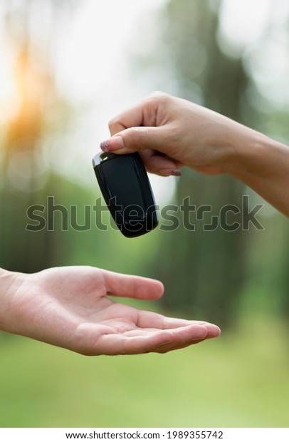 Selective focus of Female\
hands and giving car keys to customer on natural blurred green\
background. 