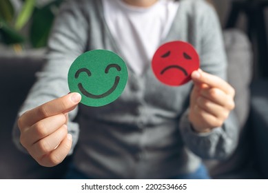 Selective focus of female hands holding happy and angry face paper sit on sofa. Feedback rating, emotional intelligence, balance emotion control, mental health assessment, bipolar disorder concept
