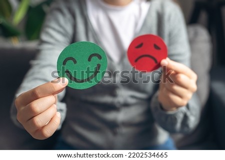 Selective focus of female hands holding happy and angry face paper sit on sofa. Feedback rating, emotional intelligence, balance emotion control, mental health assessment, bipolar disorder concept