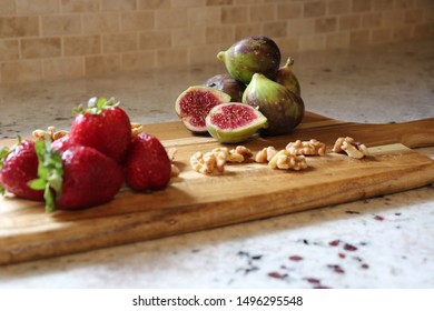 Selective focus (figs): Figs served sliced opened on a wooden board, with strawberries and nuts in the foreground. .