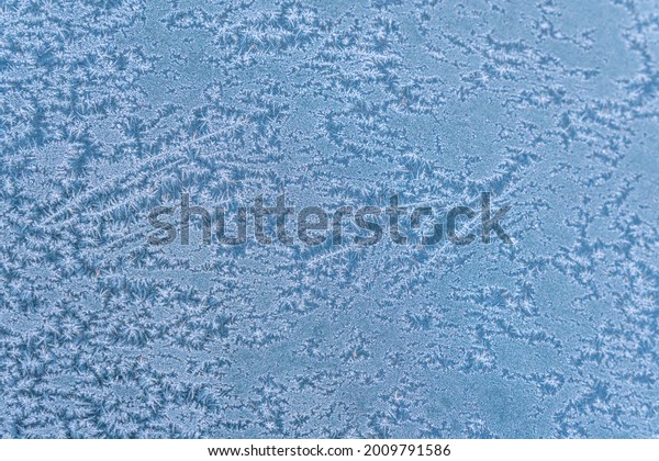 Selective focus. First frost\
on a frozen car, late autumn close-up. Beautiful abstract frozen\
microcosmos pattern. Freezing weather frost action in nature.\
Winter backdrop.