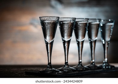 Selective focus of five shot glasses of cold vodka on wooden table, close up