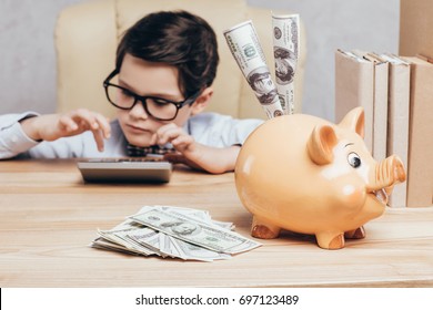 Selective Focus Of Focused Kid Using Calculator At Workplace With Piggy Bank And Cash