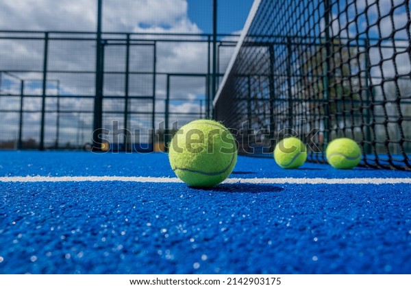 selective focus, four\
paddle tennis balls on a blue paddle tennis court close to the net,\
racket sports concept