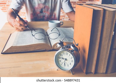 Selective focus front of work table alarm clock with stack book with blur a man reading a book - Powered by Shutterstock