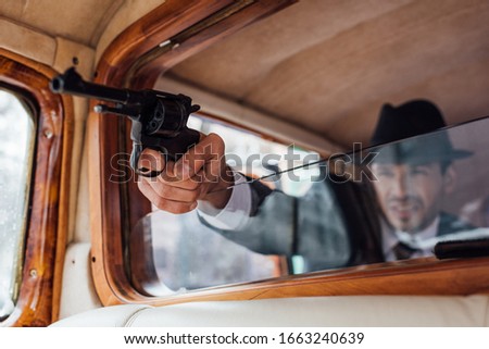 Selective focus of gangster aiming gun with outstretched hand from retro car