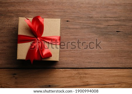 Selective focus of gift box with red ribbon and love shaped paper over rustic wooden table, top view flat lay.