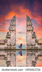 (Selective focus) A girl is posing in front of the Gate of Heaven with its reflection in the water during a stunning sunset. Bali, Indonesia.
