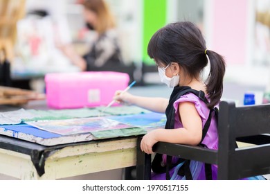 Selective Focus. Girl Wearing Cloth Face Mask Painting On Canvas. Kid Made Art Paint Watercolor. Child In Black Apron Uniform Sits On Dark Brown Wooden Chair. Children Make Crafts In Class 4 Year Old.