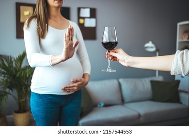 Selective focus of glass of red wine in hand of male and pregnant woman refusing it at background. Future mother leading healthy way of life and caring about health of baby. Concept of pregnancy.