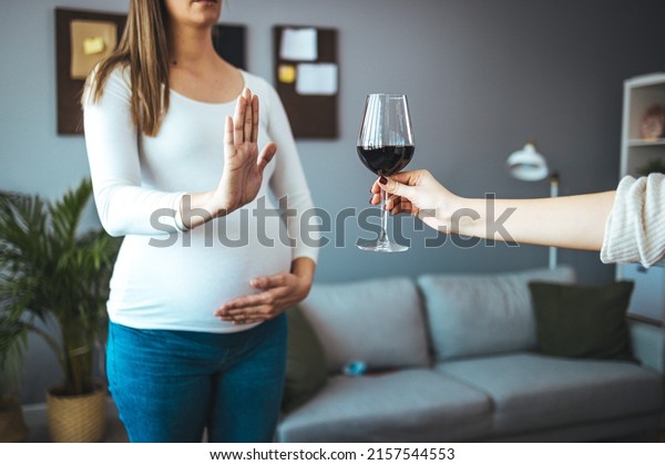 Selective focus of glass of red wine in hand\
of male and pregnant woman refusing it at background. Future mother\
leading healthy way of life and caring about health of baby.\
Concept of pregnancy.