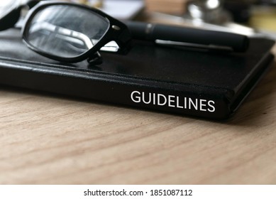 Selective Focus Of Glasses, Pen And Black Book Title Of Guidelines On Wooden Background.