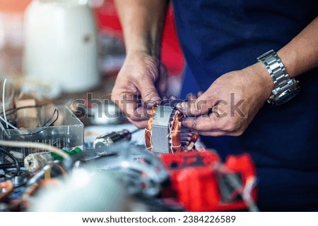 Selective focus to hand of an electric motor repairman. Mechanic is repairing an electric motor by replacing the copper coil. Electric fan motor repair work in Ban Mo area, Bangkok, Thailand.