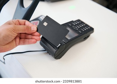 Selective focus. Hand holding black mockup plastic card with copy advertising space over credit card reader, shopping, making cashless payment in the store. Internet banking. Online cashless payment.