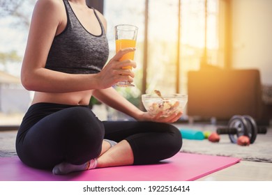 Selective focus hand holding orange juice. Fitness sport woman in fashion sportswear eating orange juice healthy salad fruit bowl. Healthy eating, dieting and exercise  concept.