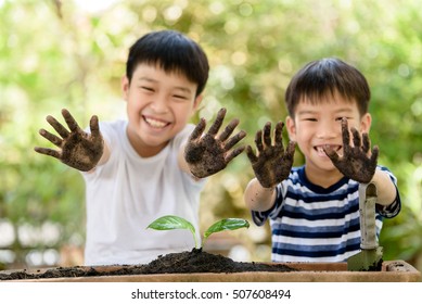 Selective focus at hand of two young Thai boy that dirty from soil after plant little seedling on black soil. Earth day and family concept