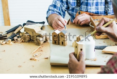 Selective focus hands painting wooden DIY house model, furniture with plan and woods in indoor house. Creative Interior Design, Hobby and Business Concept