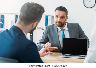selective focus of handsome advisor pointing with fingers at laptop with blank screen