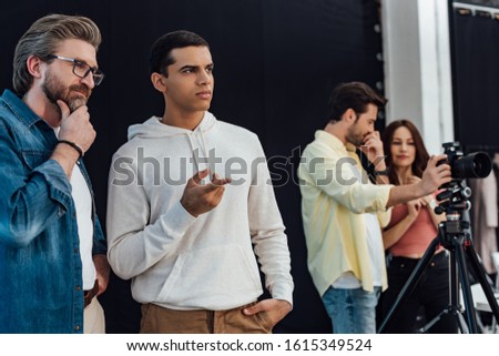 selective focus of handsome assistant pointing with finger while standing near art director in glasses
