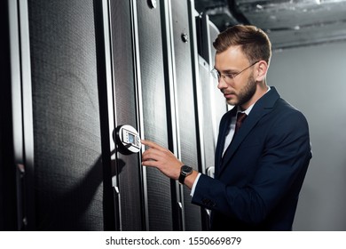 selective focus of handsome businessman in suit and glasses pointing with finger at digital panel 