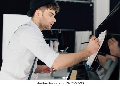 Selective Focus Of Handsome Composer Writing In Music Book While Sitting At Piano At Home