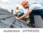selective focus of handsome handyman repairing roof with coworker 