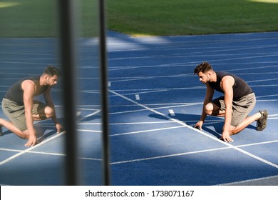 selective focus of handsome runner in start position on running track at stadium