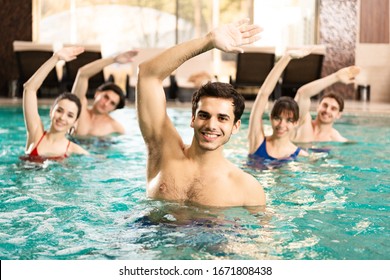 Selective focus of handsome trainer smiling at camera while exercising with people in swimming pool