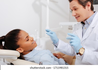 Selective Focus Of Happy Dentist Holding Dental Floss Near African American Woman In Braces