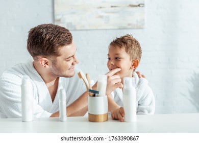 Selective Focus Of Happy Father Checking Teeth Of Cute Son Near Toiletries In Bathroom