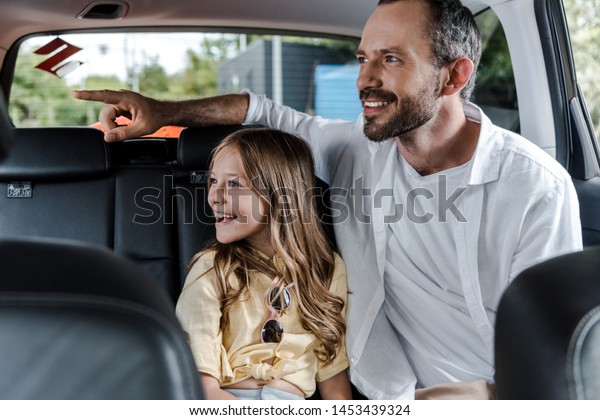 selective focus of happy father pointing with finger\
near daighter in car 