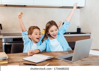 Selective Focus Of Happy Kids With Hands Above Head Looking At Laptop While Having Video Chat At Home