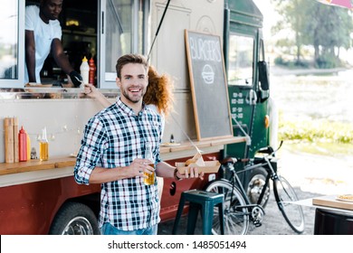 Selective Focus Of Happy Man Holding Bottle With Beer And Carton Plate With Street Food Near Woman And African American Man In Food Truck 