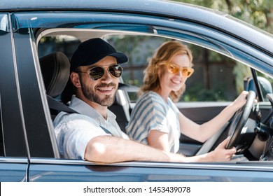 selective focus of happy man in sunglasses smiling near attractive woman driving car  - Shutterstock ID 1453439078