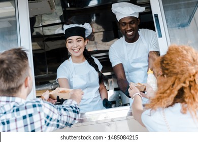 selective focus of happy multicultural chefs giving carton plates with food to customers  - Powered by Shutterstock