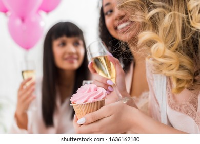 Selective Focus Of Happy Multicultural Girlfriends Having Fun With Champagne And Cupcake During Bachelorette Party 