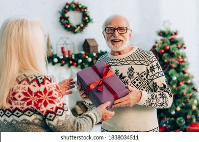 selective focus of happy senior man looking at camera while presenting christmas gift to wife - Powered by Shutterstock