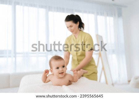 Selective focus of happy smiling infant boy having legs massage. Female doctor doing gymnastics and foot massage to toddler baby. Nurse in uniform doing orthopedic leg exercises to cute child.