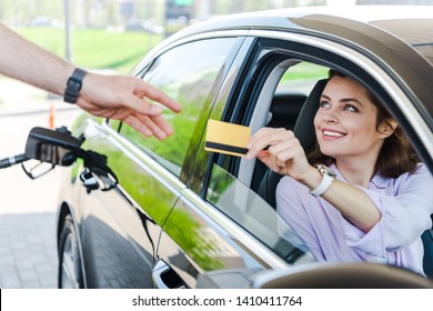 selective focus of happy woman sitting in car and giving credit card to worker at gas station  - Powered by Shutterstock