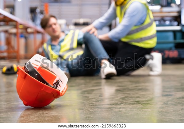 Selective focus at hat, Men worker feel painful\
and hurt from the accident that happen inside of industrial factory\
while his co-worker come to give emergency assistance and help.\
Accident in factory.