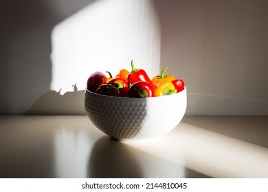 Selective Focus Horizontal Shot Of Red, Orange And Yellow Mini Bell Peppers In White Bowl Set In Dappled Light On Wooden Table 