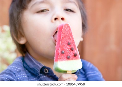Selective focus of hugry boy enjoyig eating watermelon ice cream in hot sunny day on summer, Blurry kid face licking watermelon ice cream sticks at the park, Picnic food for summer concept