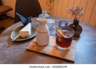 Selective focus at ice cold brew coffee beside classic cheese cake on wooden round table. Cozy interior cafe atmosphere.