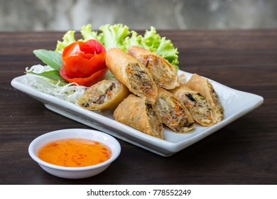 Selective focus image Fried Veg. Spring rolls on white dish with sweet sauce on wooden table.
