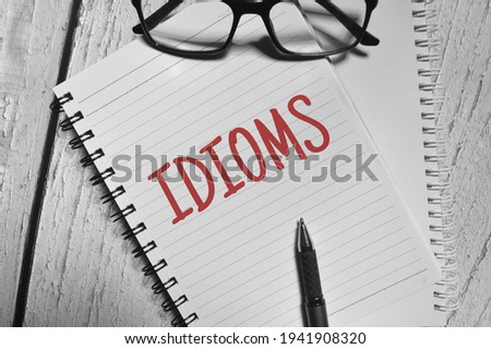 Selective focus image of pen and spectacles with idioms wording over a wooden background.
