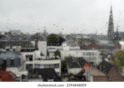 A selective focus image of raindrops on a window overlooking a defocused urban view of a city skyline on a wet day.